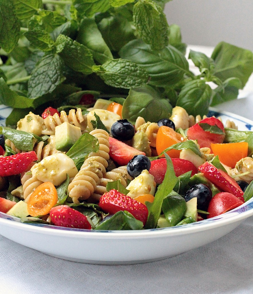 pastasalaatin joukossa on mustikoita ja mansikoita taustalla näkyy minttu- ja basilikayrttejä